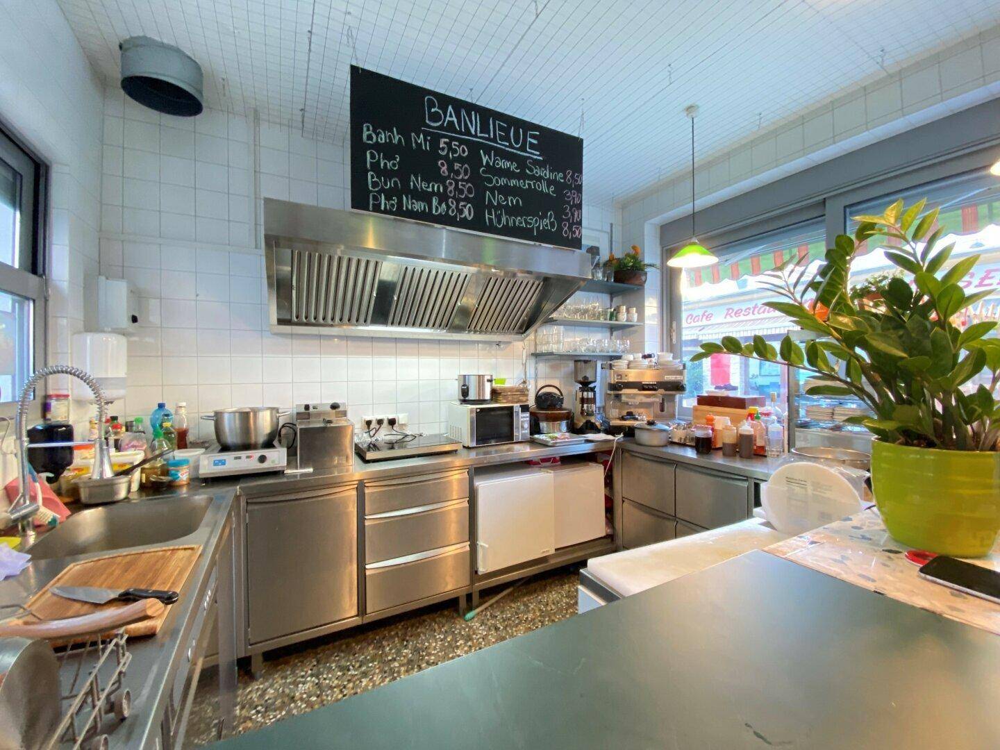 Professionelle Edelstahlküche mit Dunstabzugshaube, Fliesenwänden und Arbeitsflächen für Gastronomiebetrieb.