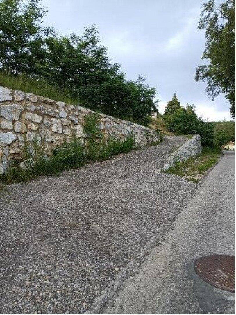 Schotterweg führt entlang einer Natursteinmauer bergauf in ländlicher Umgebung.