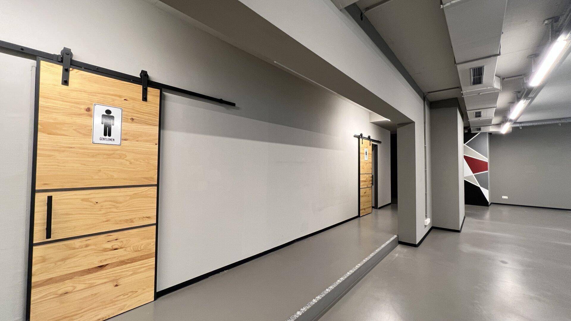 Flur mit modernen Schiebetüren aus Holz, die zu den Toiletten führen, und industrieller Deckenbeleuchtung.