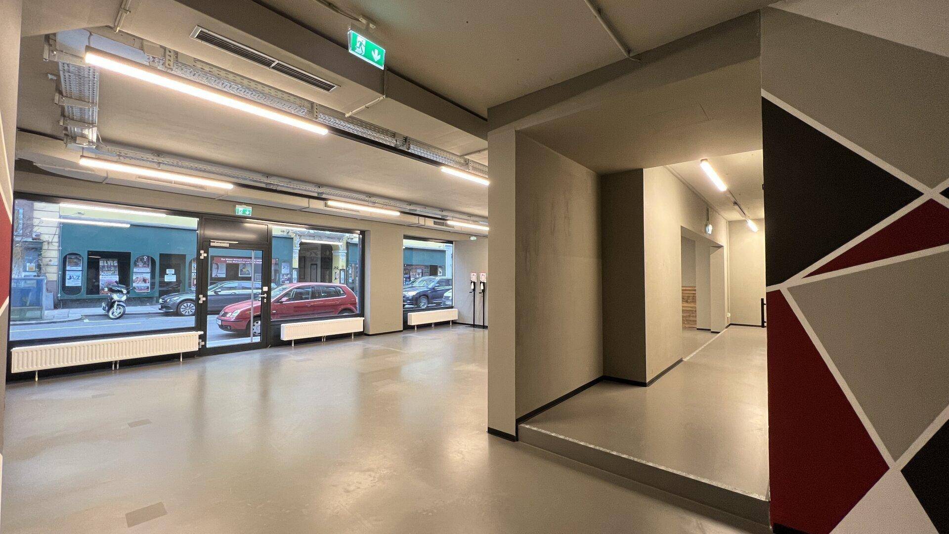 Heller Geschäftsraum mit großen Fenstern zur Straße und einem modernen geometrischen Wanddesign.