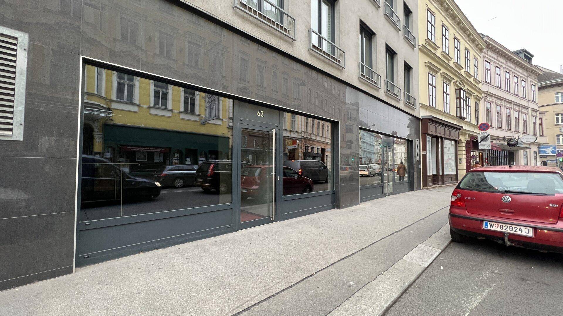 Moderne Geschäftsfassade mit großen Glasfenstern, die die Straße und umliegende Gebäude widerspiegeln.