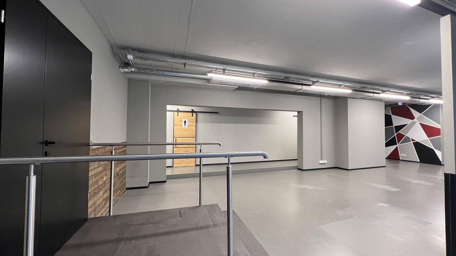 Geräumiger Geschäftsraum mit erhöhter Plattform, modernen Schiebetüren und geometrischer Wandgestaltung.