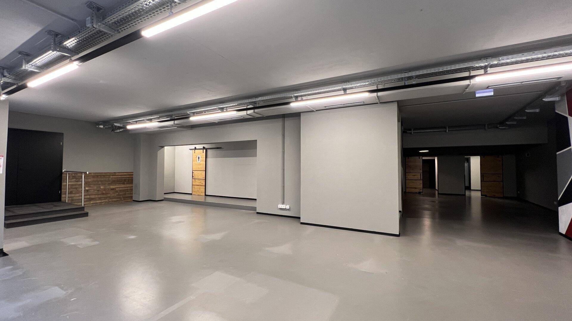 Großer, leerer Gewerberaum mit industrieller Deckenbeleuchtung und grauen Böden, bereit für den Ausbau.
