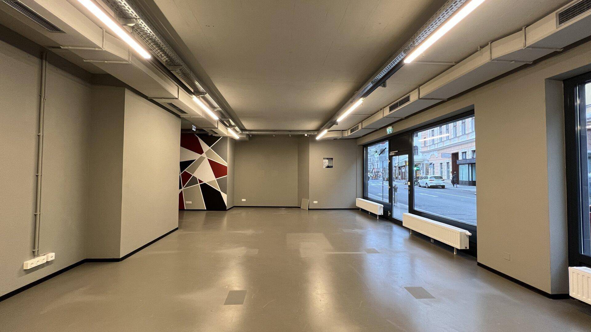 Großer, leerer Geschäftsraum mit minimalistischem Design, großen Fenstern und einer geometrischen Akzentwand.