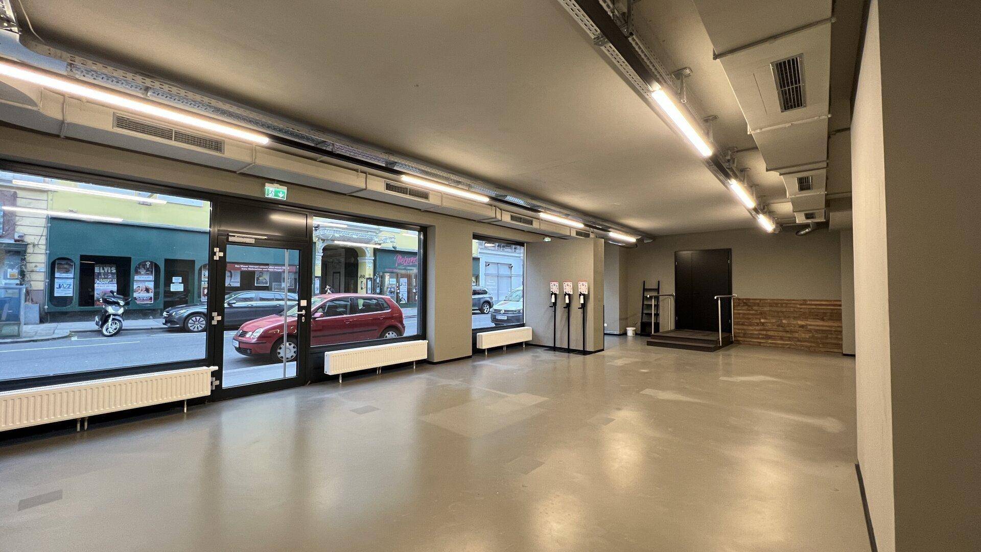 Heller Geschäftsraum mit großen Schaufenstern, die den Blick auf die Straße freigeben, und moderner Beleuchtung.
