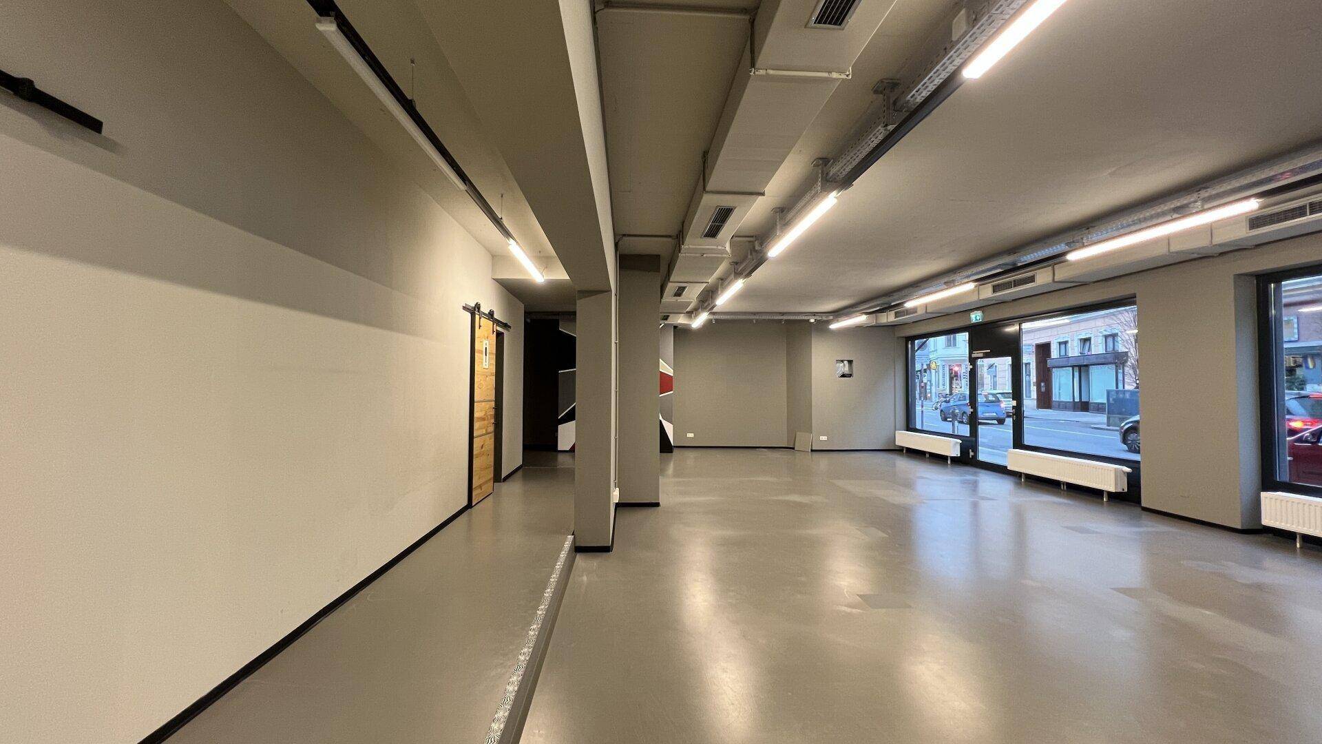 Leerer Geschäftsraum mit moderner Innenausstattung, großen Fenstern und einer Schiebetür aus Holz im Hintergrund.