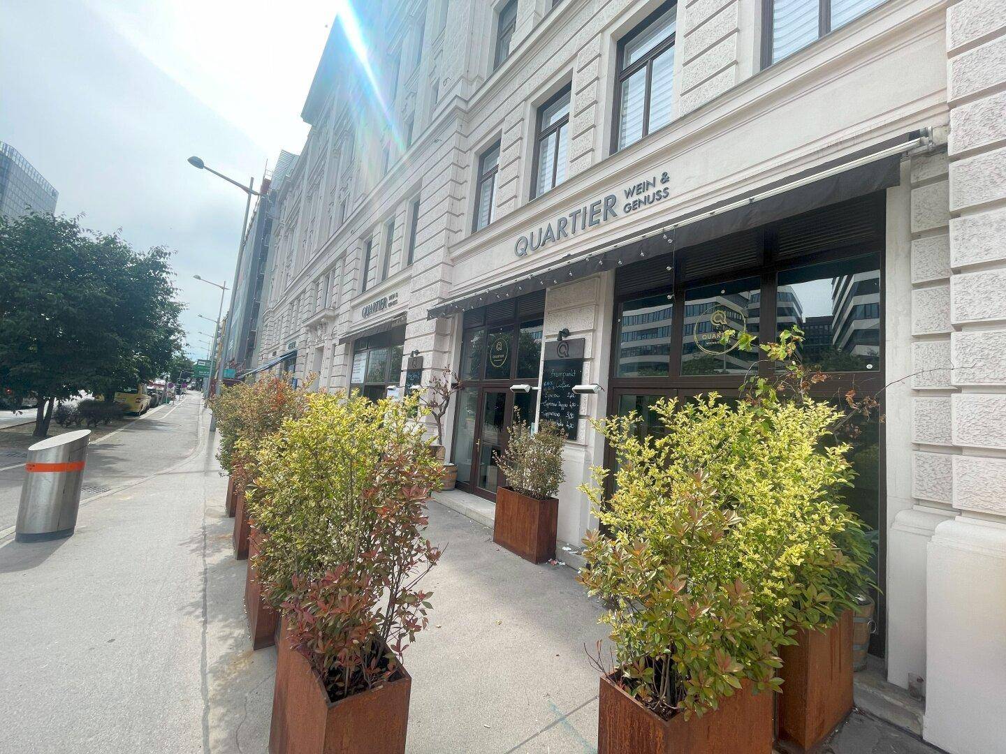Elegante Fassade des Gebäudes mit Geschäftsbezeichnung und dekorativen Pflanzenkübeln entlang des Bürgersteigs.