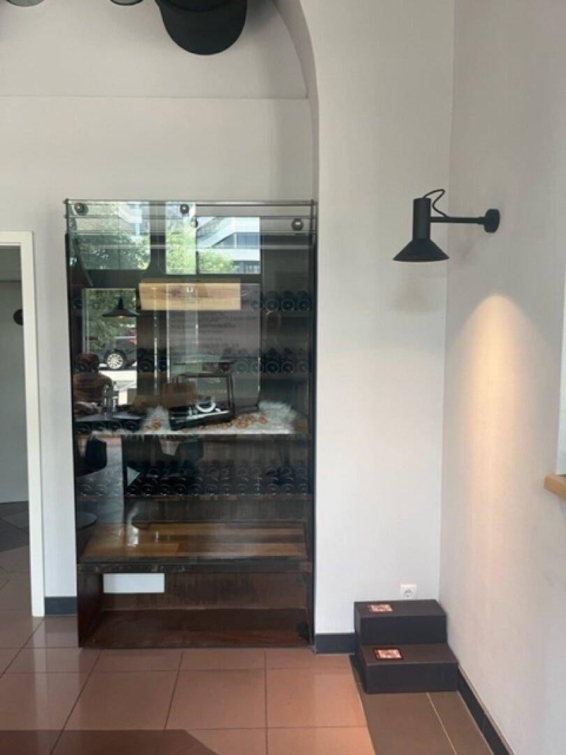 Glasvitrine mit Ausstellungsstücken an einer hellgrauen Wand und gefliestem Boden.