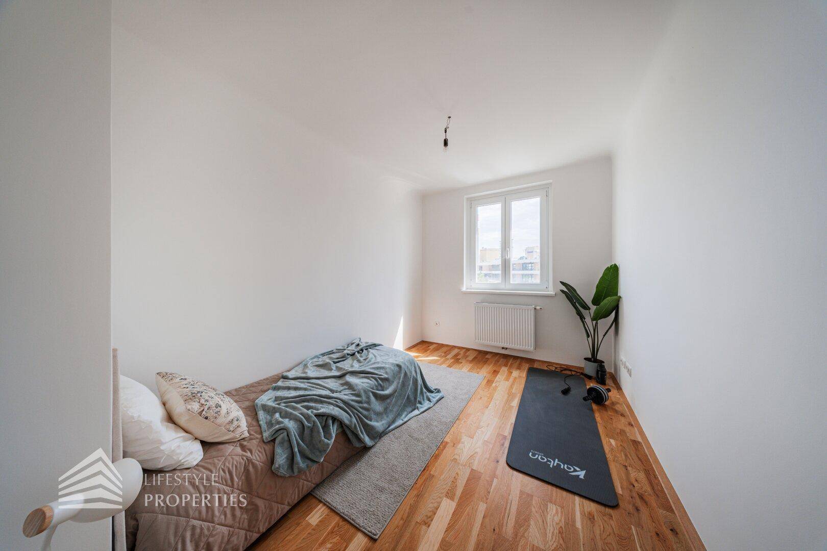 Helles Schlafzimmer mit Holzboden, Fenster und Platz für ein Doppelbett.