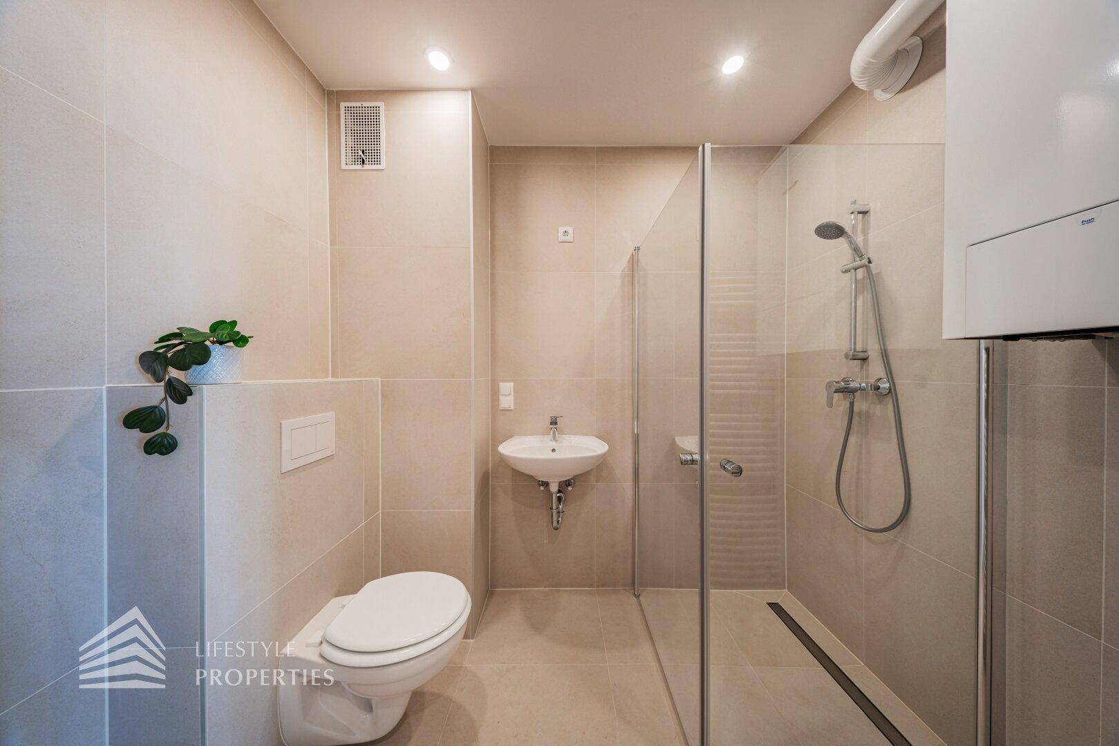 Modernes Badezimmer mit Dusche, WC und Waschbecken, komplett gefliest.