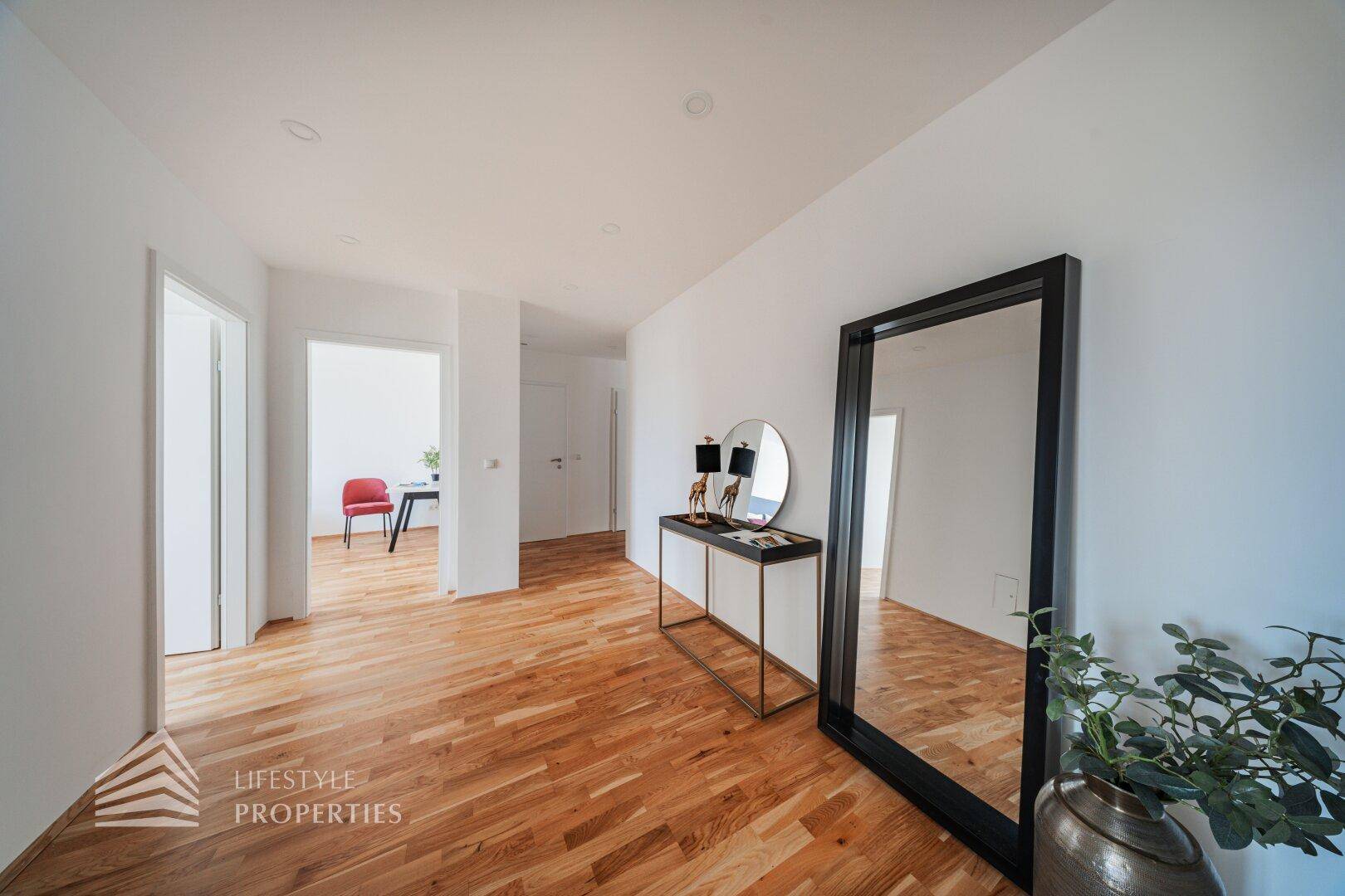 Heller Flur mit Holzboden und großem Spiegel, verbindet die Wohnbereiche.