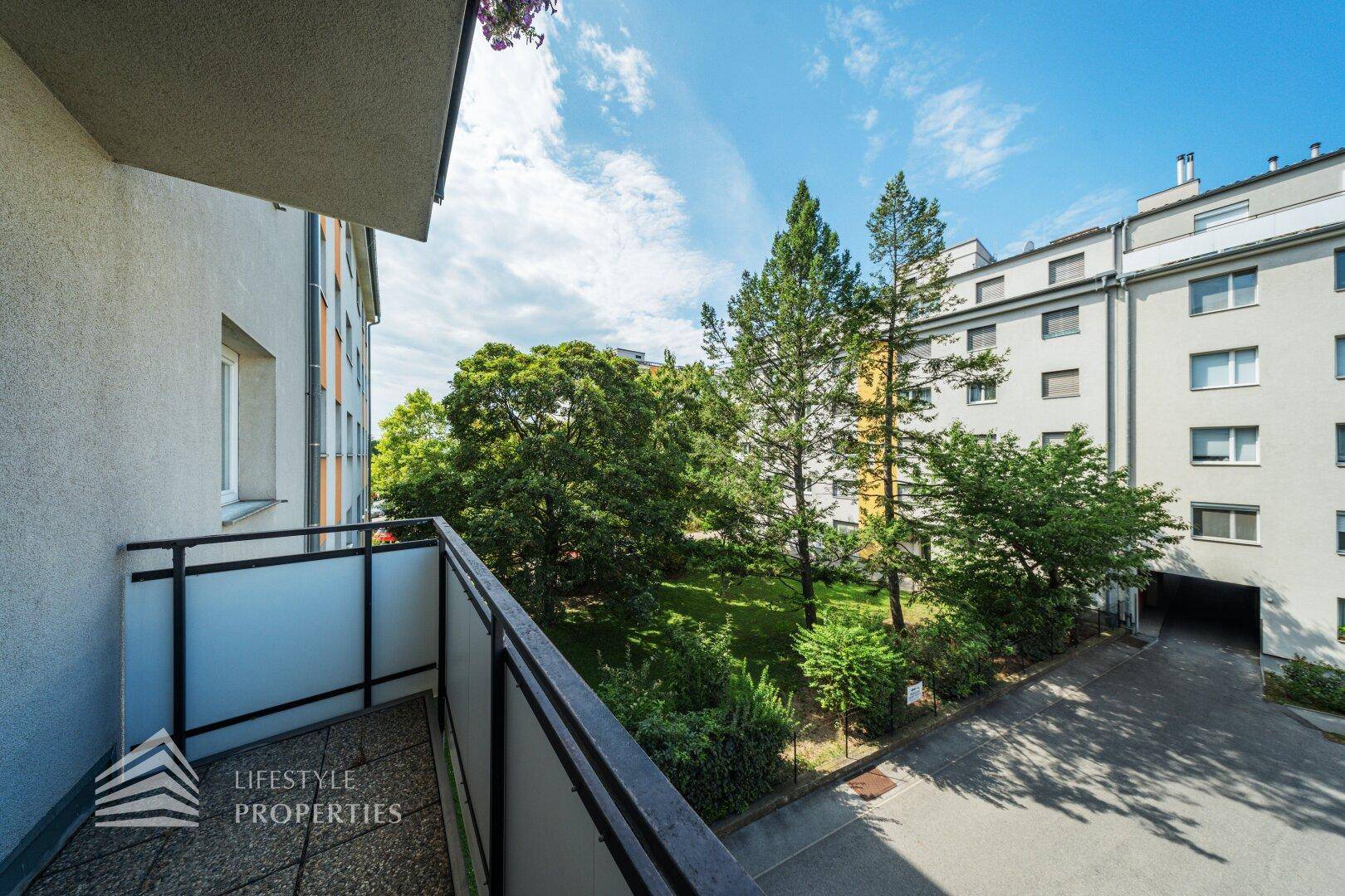 Balkon mit seitlichem Blick auf den begrünten Innenhof und die Nachbarschaft.