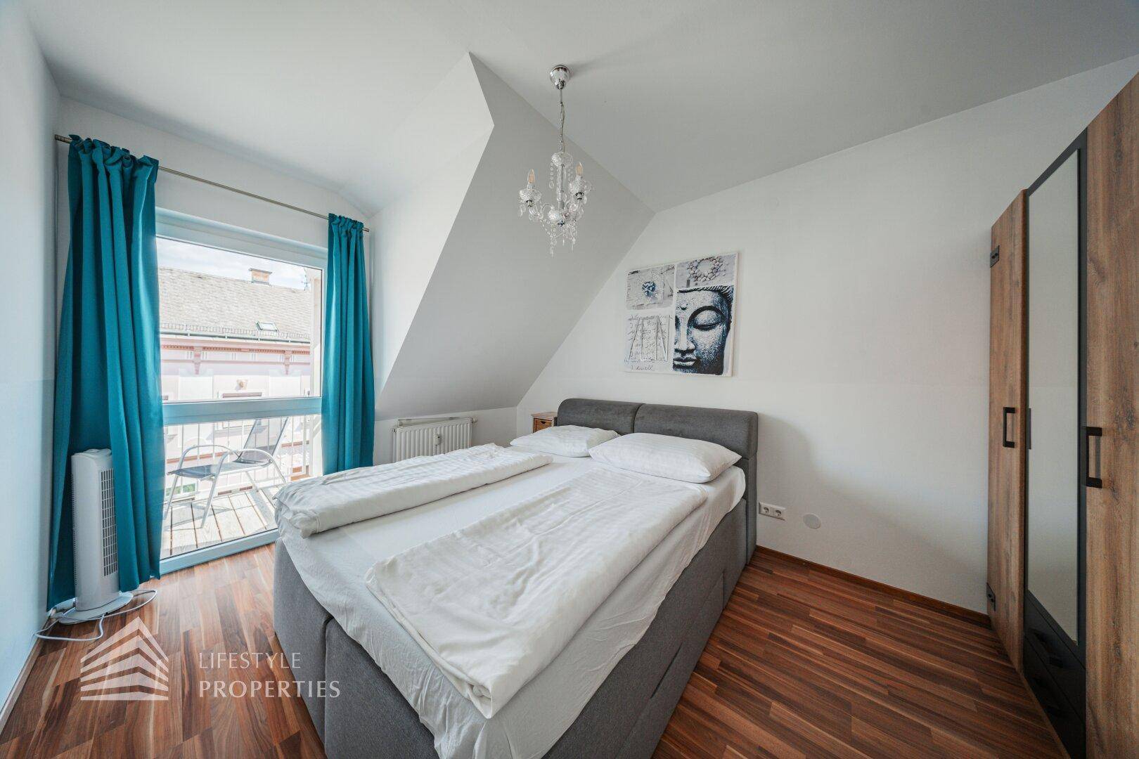 Gemütliches Schlafzimmer im Dachgeschoss mit Holzboden, Doppelbett und Zugang zu einem Balkon.