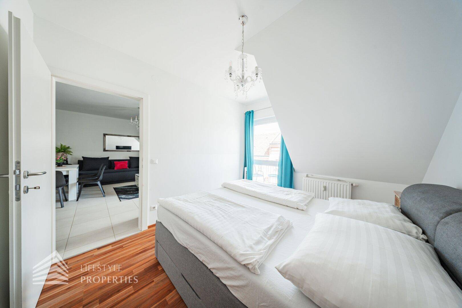 Schlafzimmer mit Holzboden und Blick durch die offene Tür in den angrenzenden Wohnbereich.