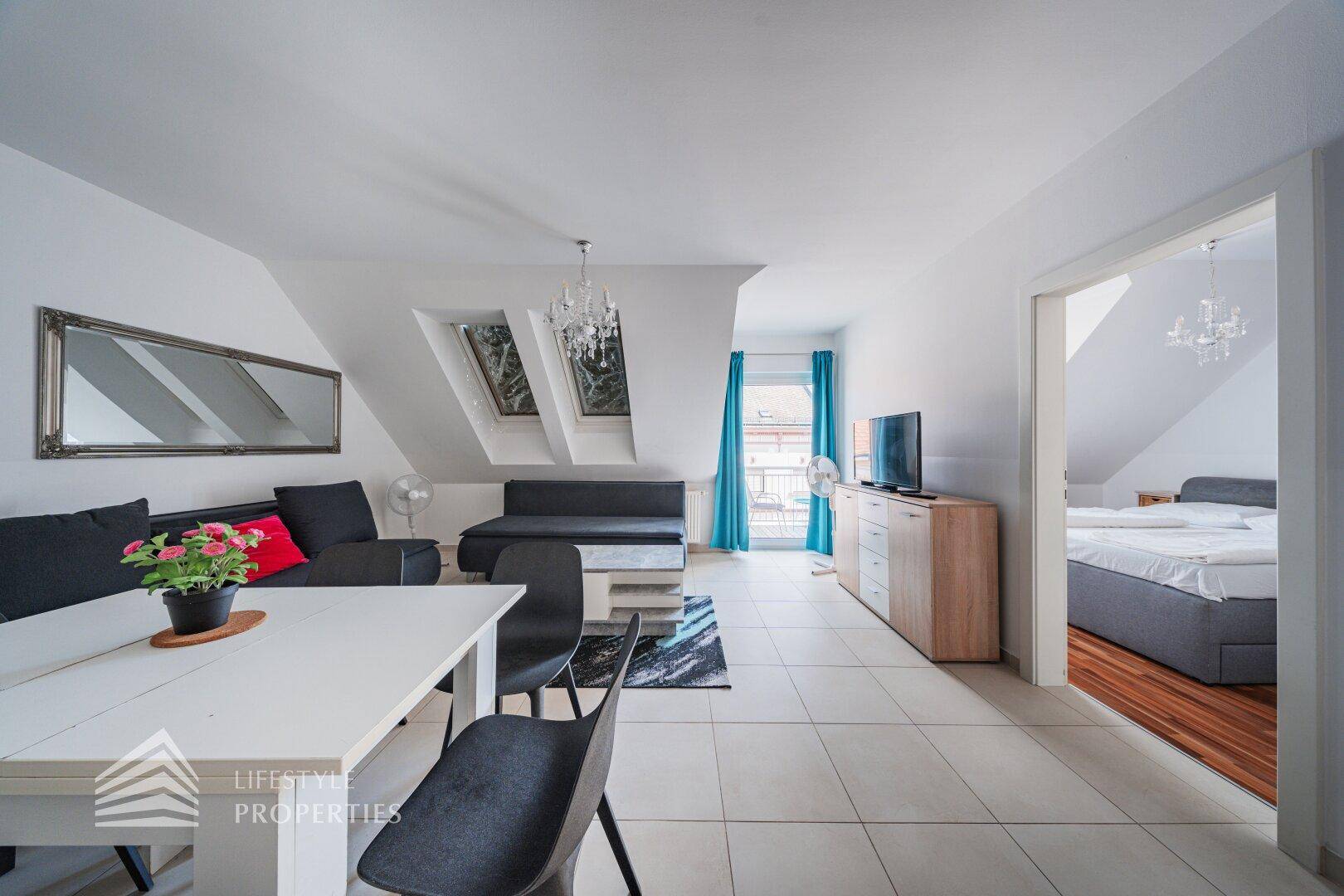 Heller Wohn- und Essbereich mit Fliesenboden, Dachfenstern und Blick in das angrenzende Schlafzimmer.