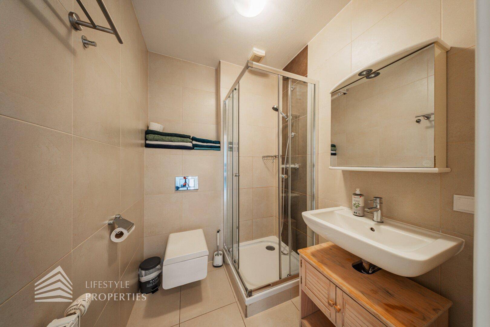 Modernes Badezimmer mit Duschkabine, wandhängendem WC und Waschbecken auf einem Holzunterschrank.