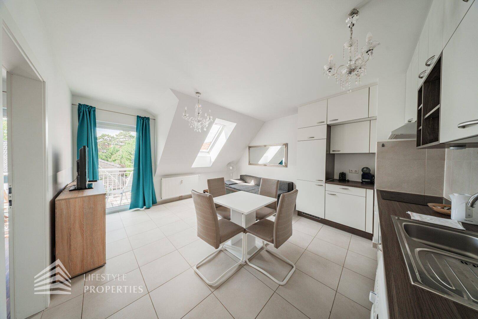 Offener Wohnbereich mit integrierter Küche, Esstisch und Zugang zu einem Balkon.