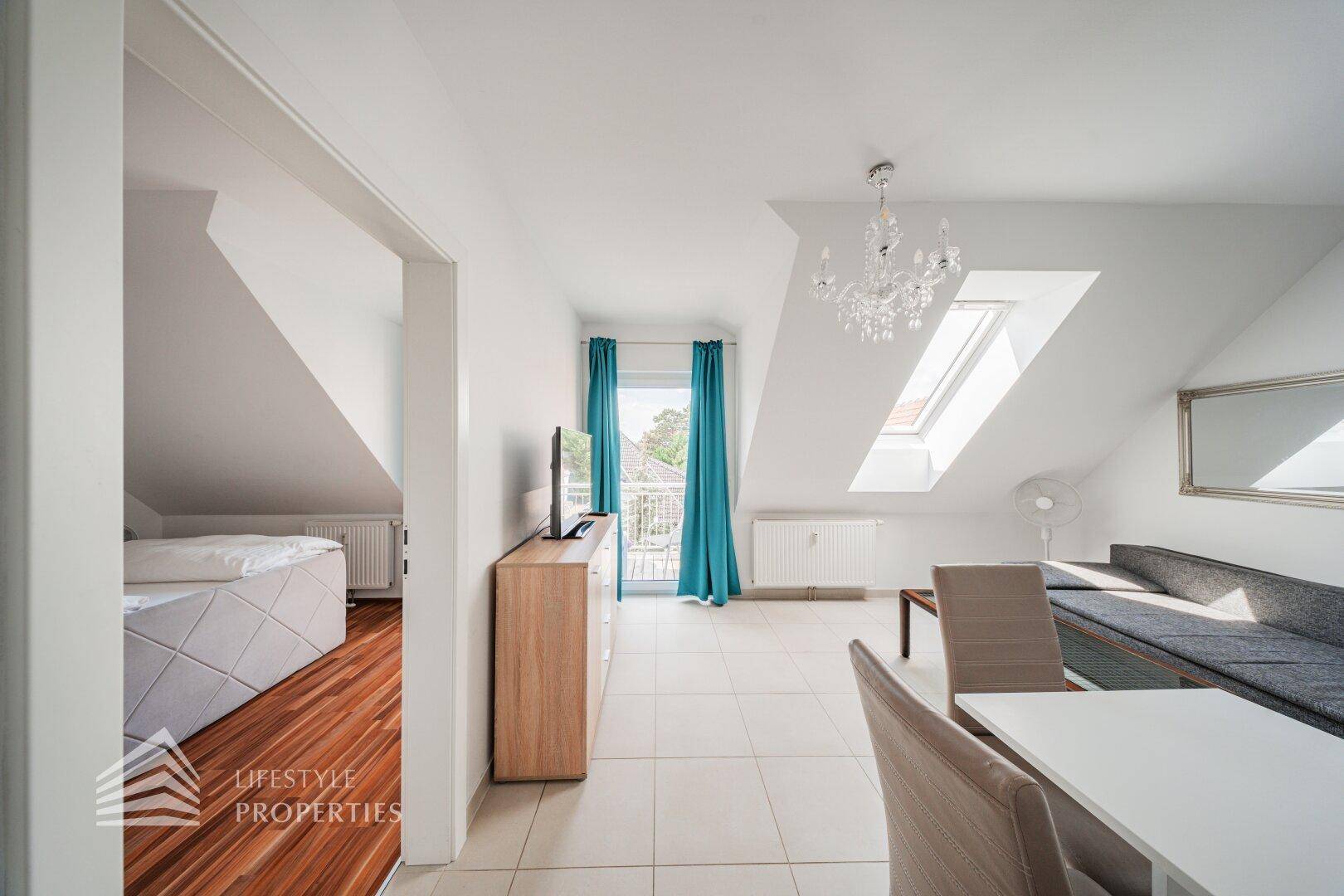 Wohnbereich mit Fliesenboden, Dachfenstern und Blick in das angrenzende Schlafzimmer.