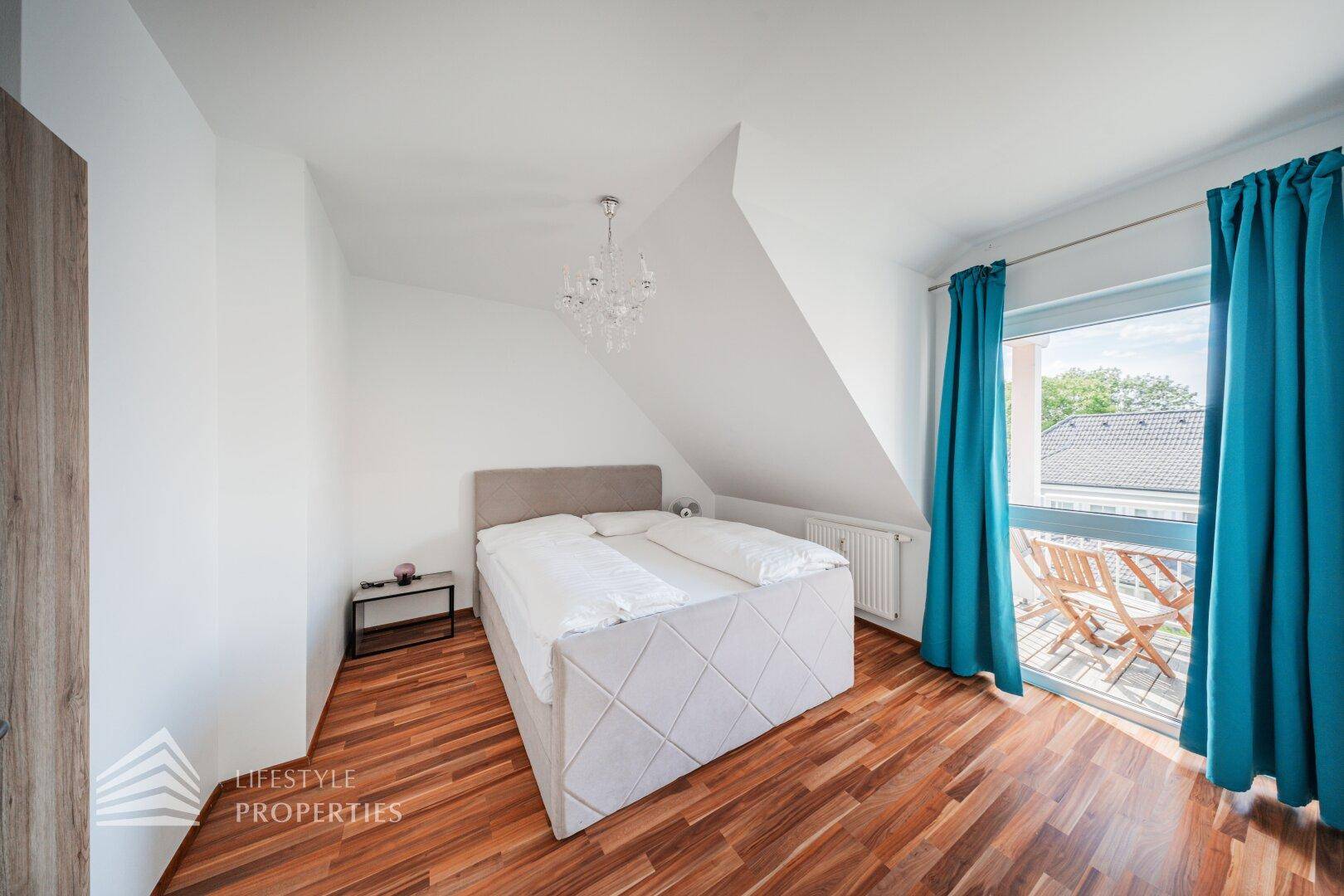 Helles Schlafzimmer im Dachgeschoss mit Holzboden, Doppelbett und Zugang zu einem Balkon.