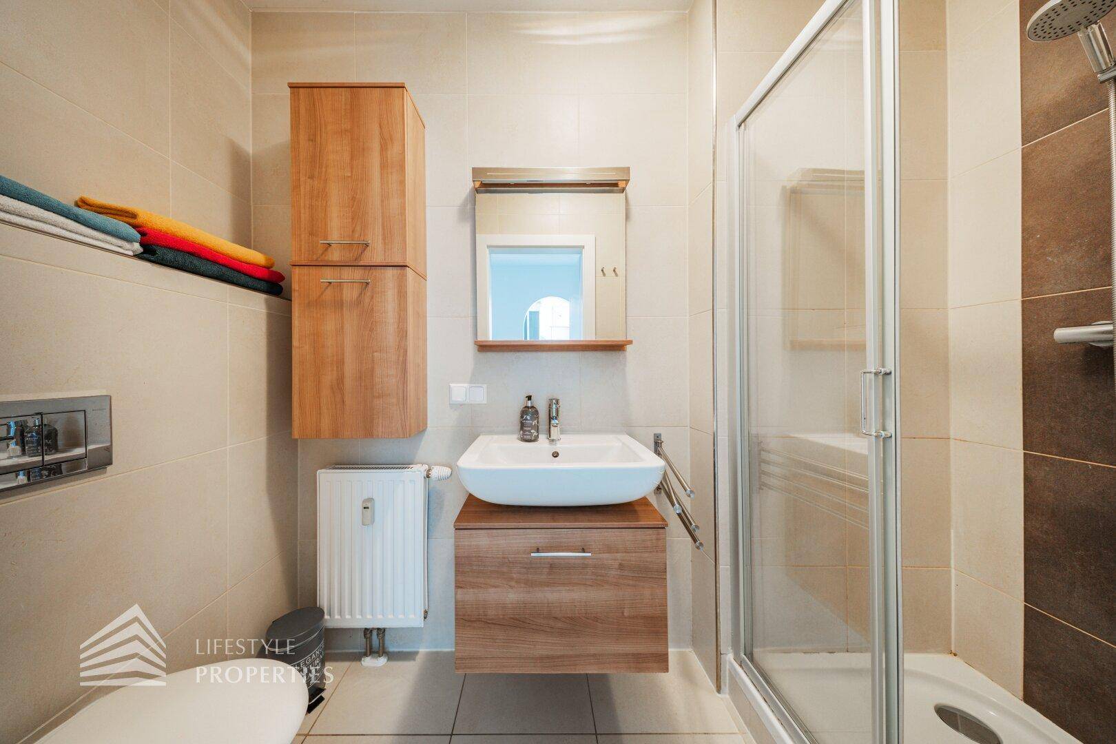 Modernes Badezimmer mit Duschkabine, wandhängendem WC und Waschbecken auf einem Holzunterschrank.