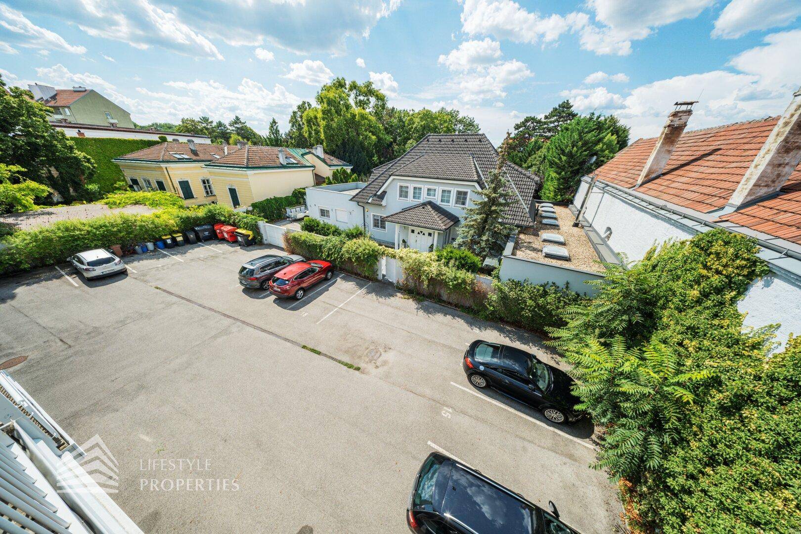 Außenansicht des Parkplatzes mit mehreren Autos und umgebender Vegetation unter blauem Himmel.