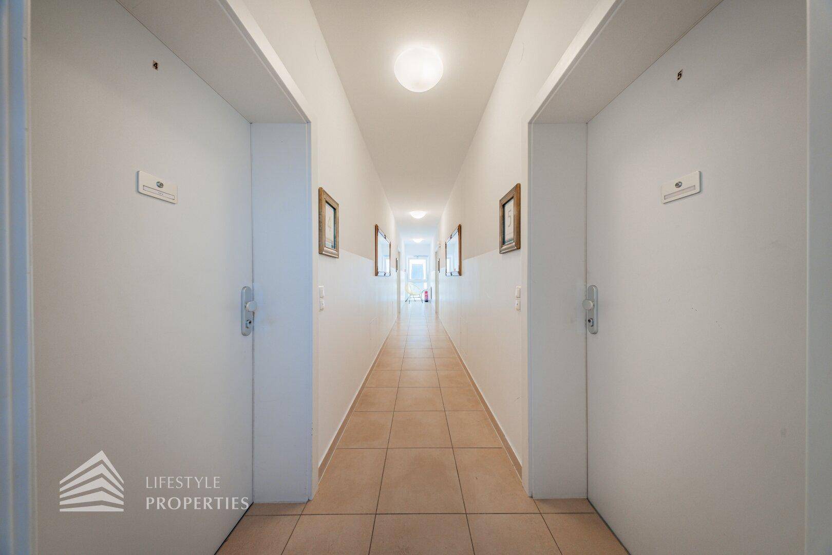 Langer, heller Flur mit Fliesenboden und Türen zu den Apartments, gut beleuchtet und einladend.
