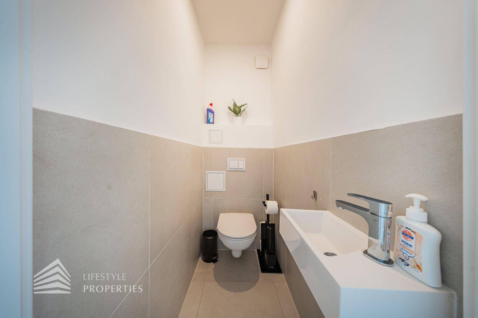 Modernes Gäste-WC mit wandhängender Toilette und stilvollem Waschbecken, halbhoch gefliest.