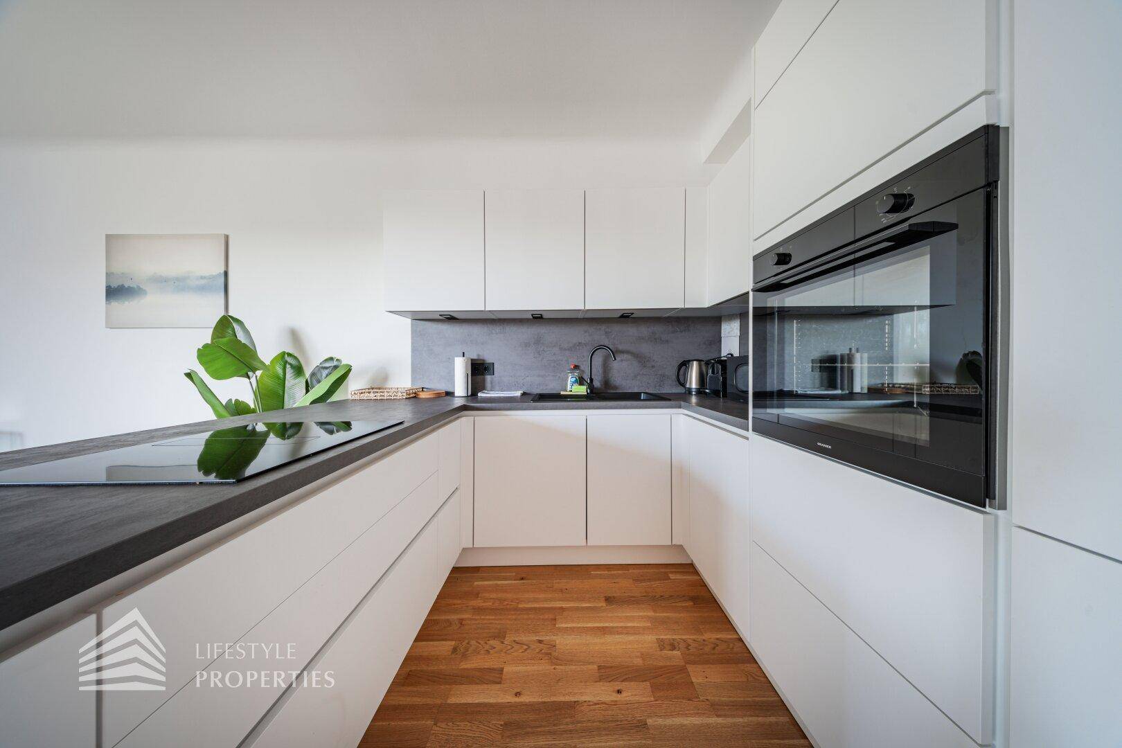 Moderne Einbauküche mit weißen Fronten, dunkler Arbeitsplatte, integriertem Backofen und Induktionskochfeld.