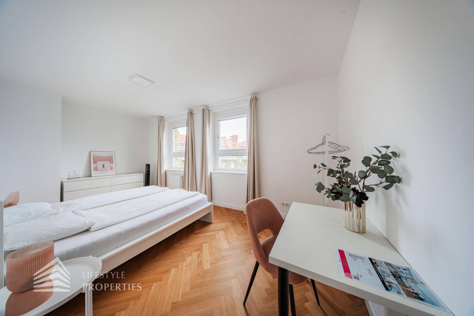 Schlafzimmer mit hellem Fischgrätparkett, Doppelbett und Schreibtisch am Fenster.
