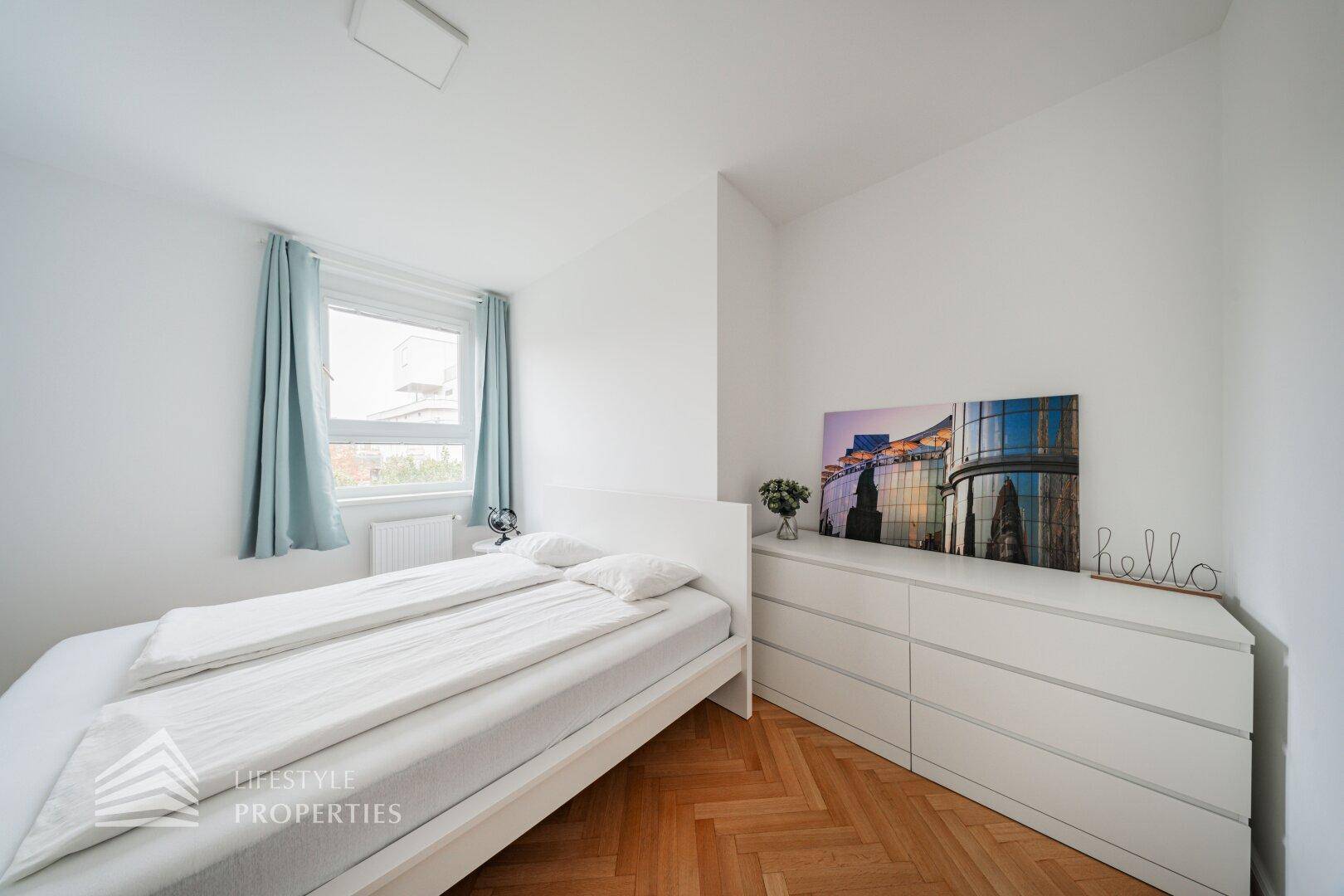 Schlafzimmer mit Doppelbett, blauen Vorhängen und moderner Kommode.