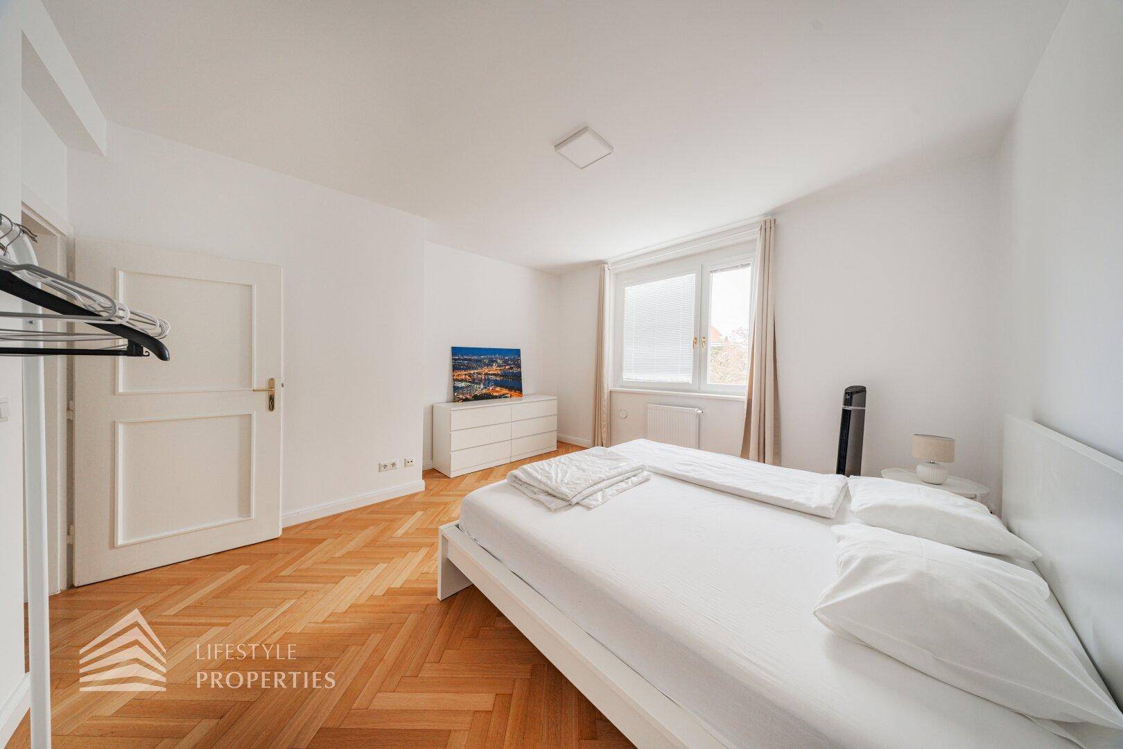 Schlafzimmer mit Doppelbett, Fischgrätparkett und weißer Kommode.