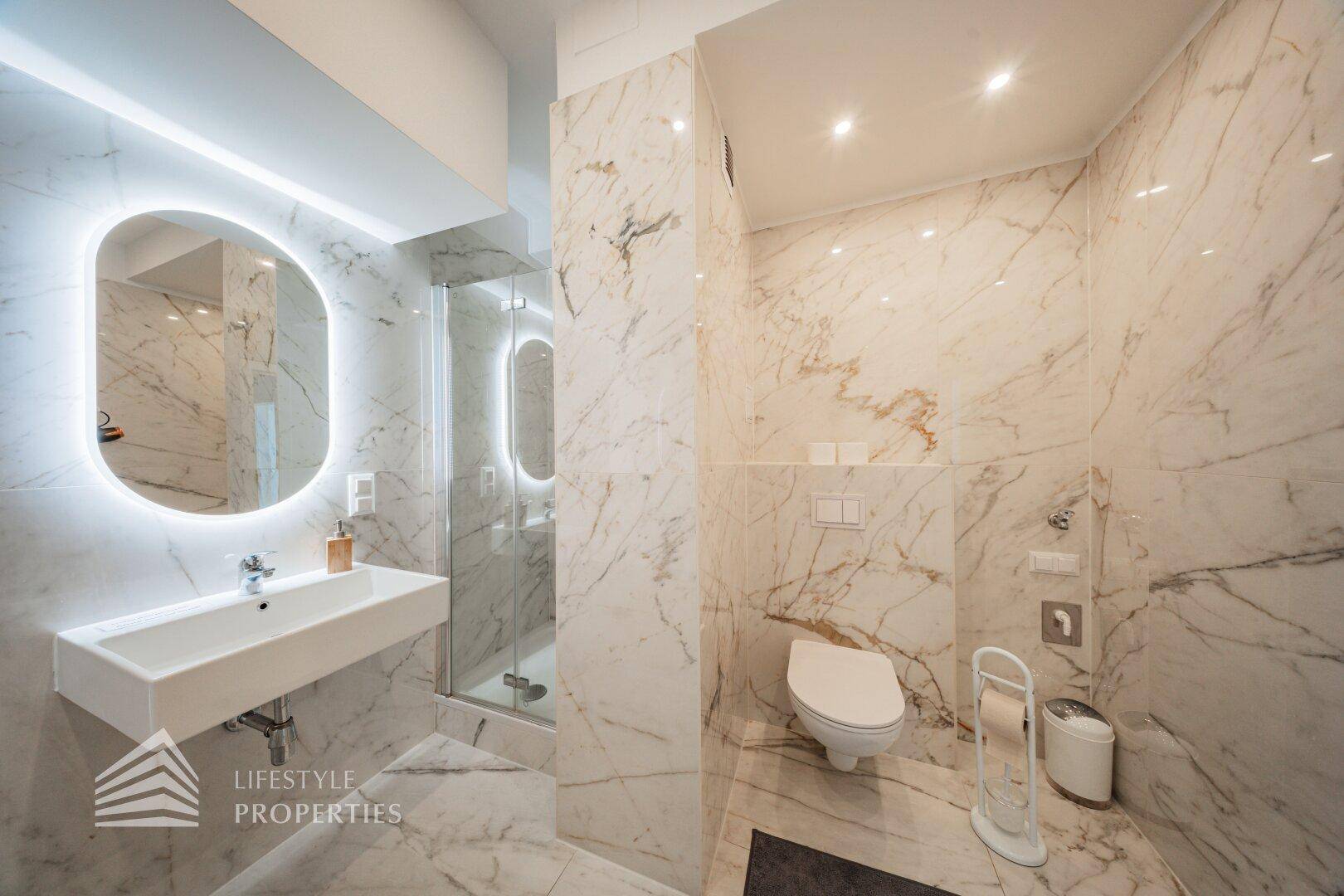 Elegantes Badezimmer mit Marmorfliesen, Dusche und modernem Waschtisch.