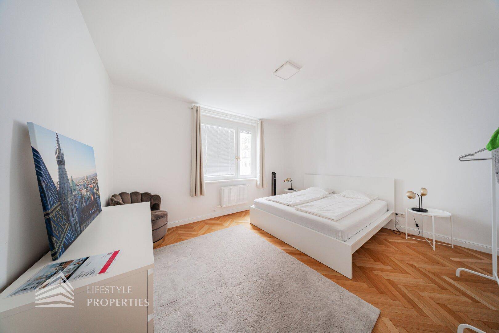 Geräumiges Schlafzimmer mit Fischgrätparkett, Doppelbett und Teppich.