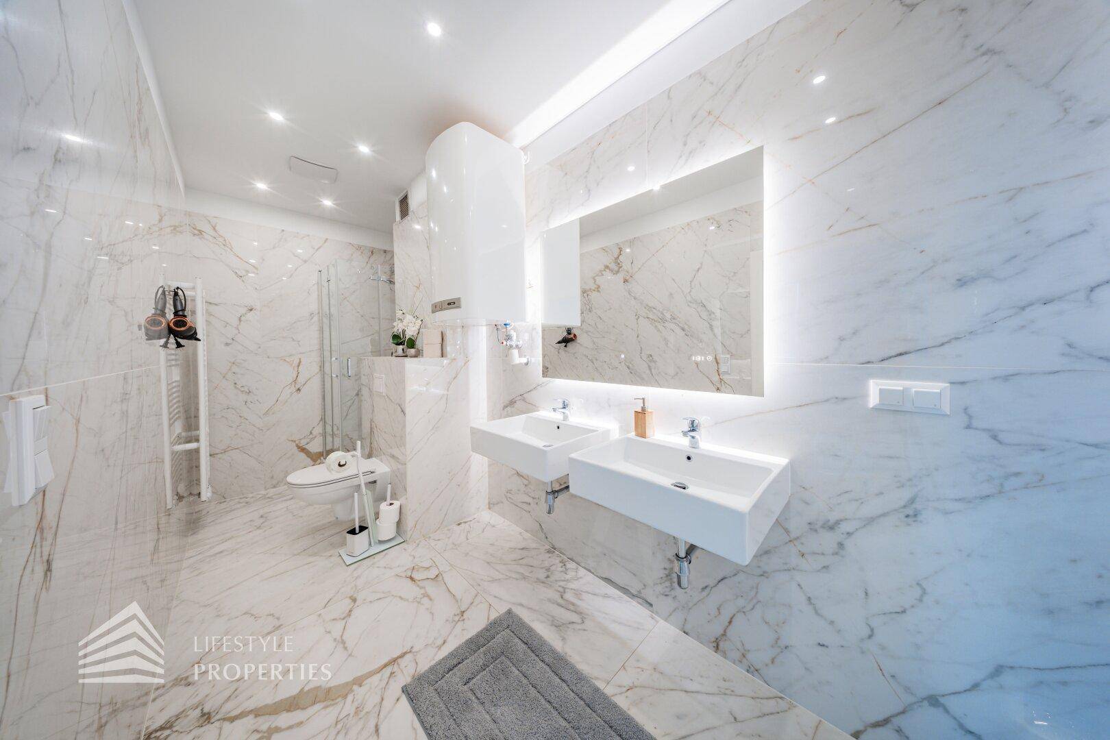 Luxuriöses Badezimmer mit doppelten Waschbecken, Marmorfliesen und großer Spiegelfläche.