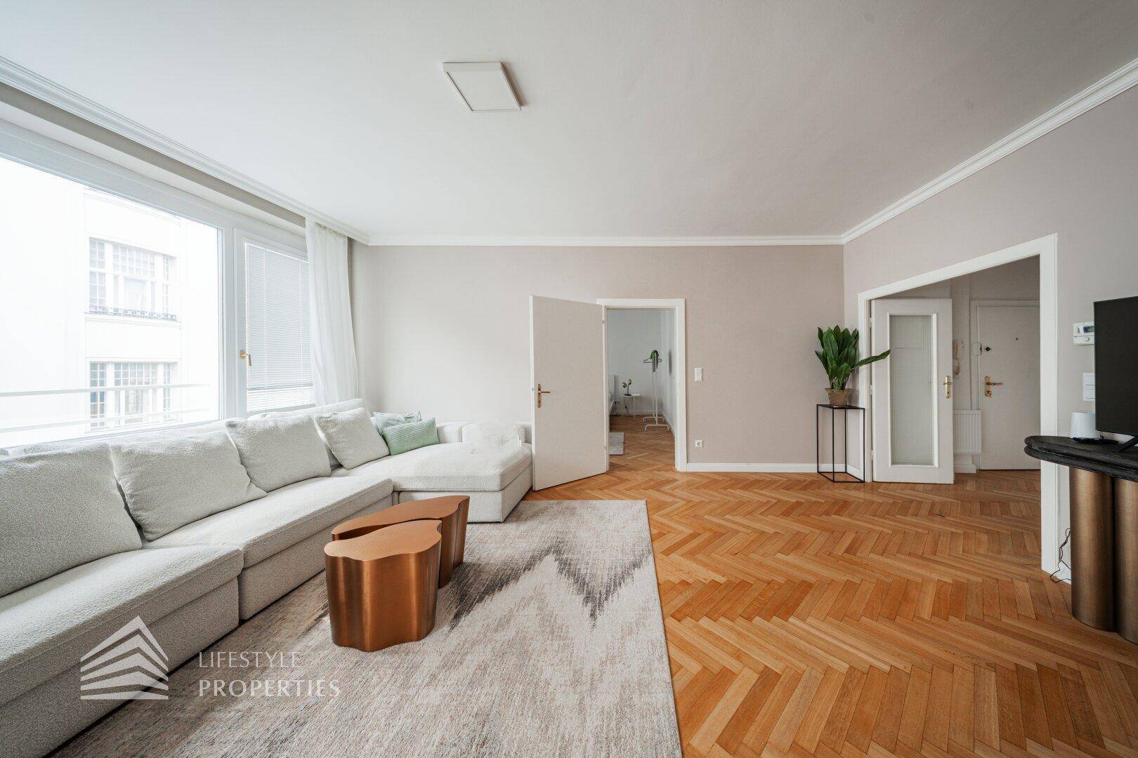 Heller Wohnbereich mit großem Sofa, Teppich und Fischgrätparkett.