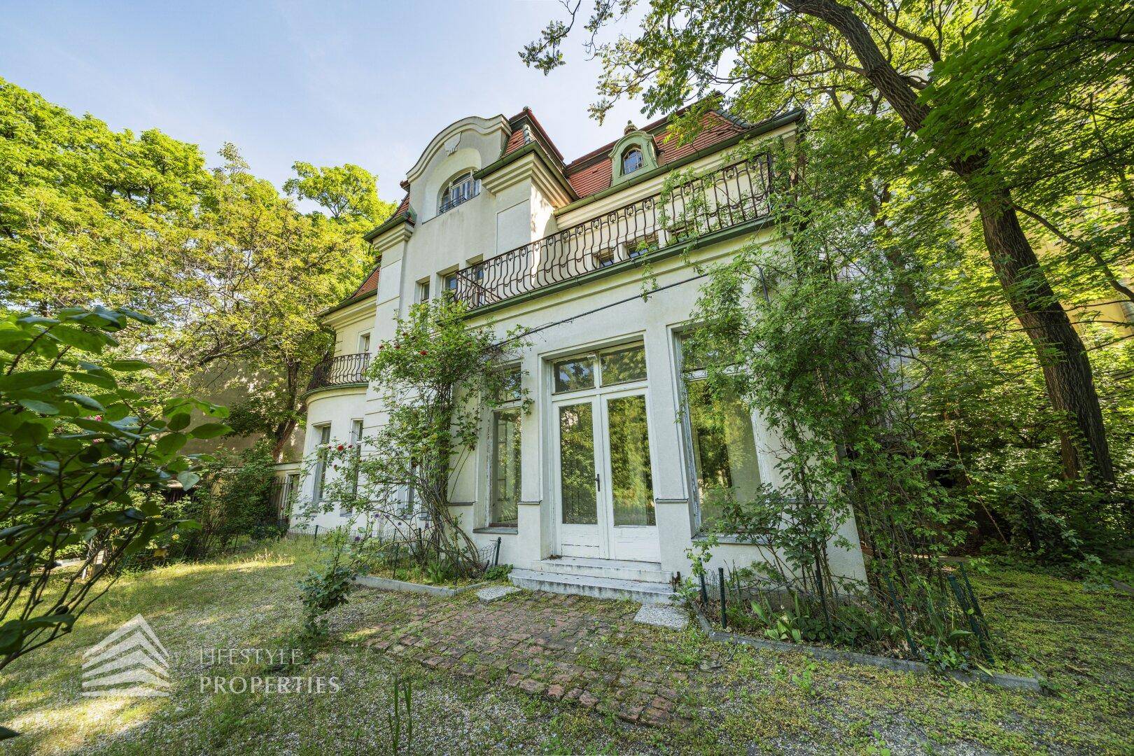 Historische Villa mit charmantem Gartenbereich und üppiger Vegetation unter strahlendem Sonnenschein.