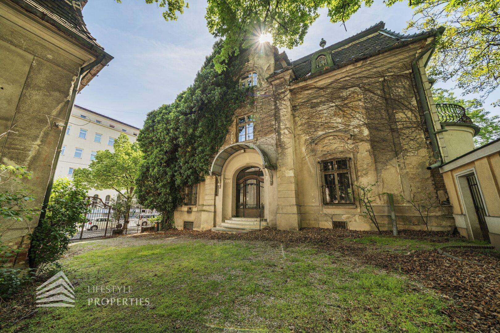 Seitlicher Eingangsbereich einer historischen Villa mit bewachsenen Mauern und grünem Vorgarten.