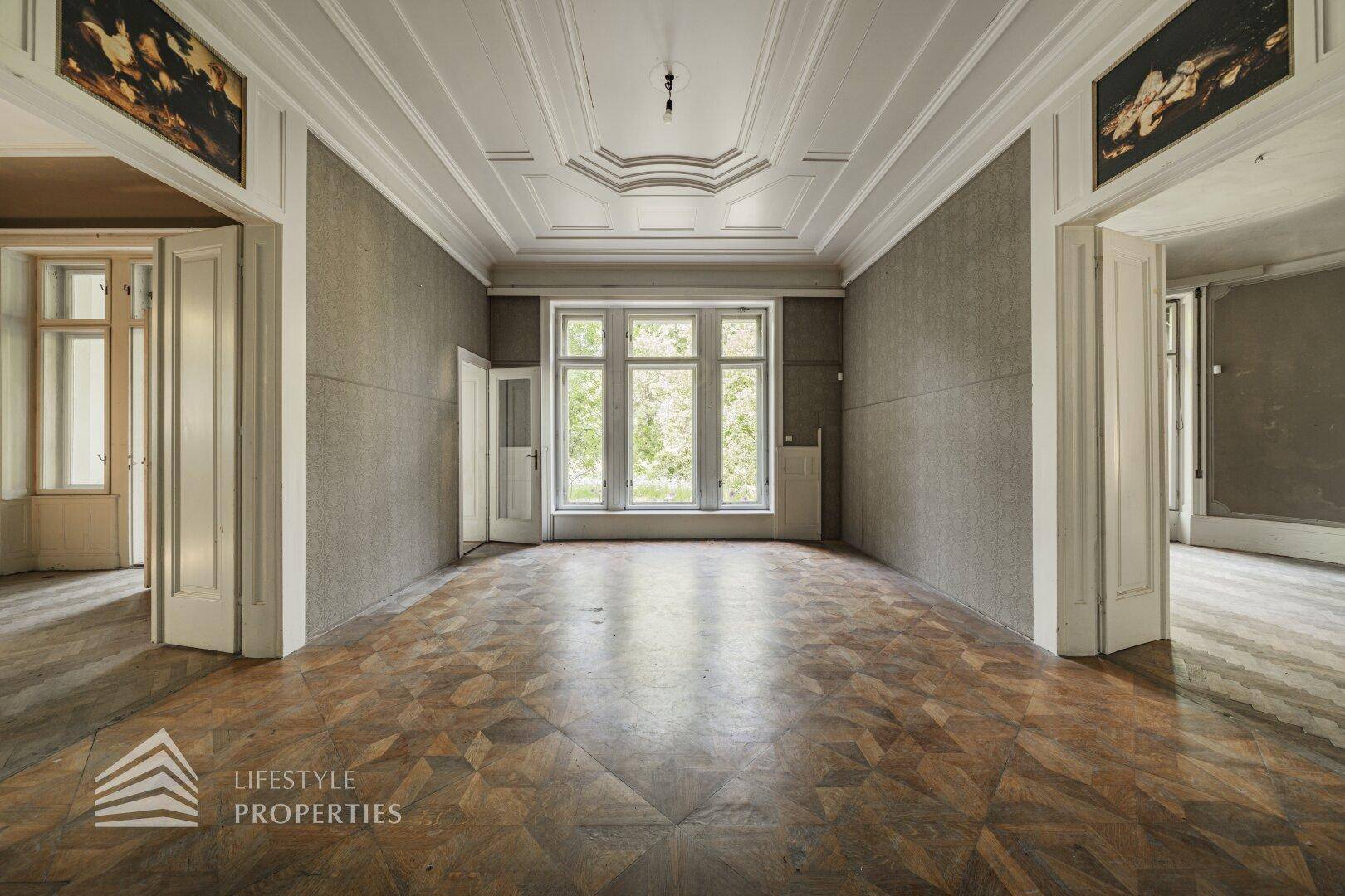 Großzügiger Raum mit aufwendiger Stuckdecke und geometrischem Parkettboden, ideal für eine stilvolle Gestaltung.