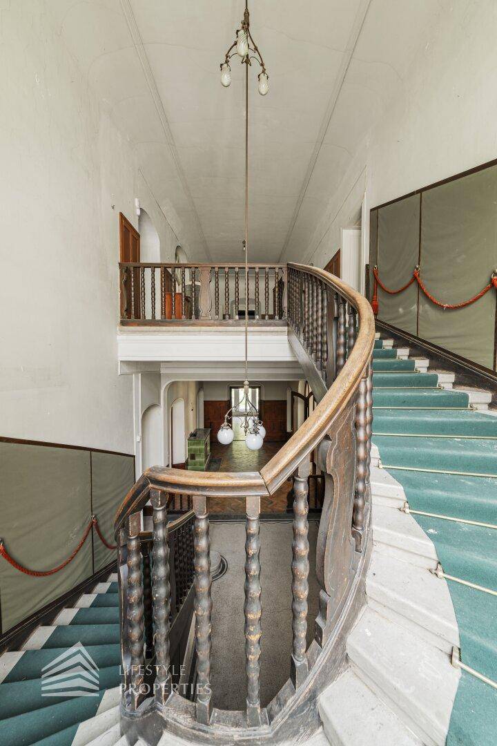 Elegantes Treppenhaus mit geschwungenem Holzgeländer und Teppichläufer, der den historischen Charme bewahrt.