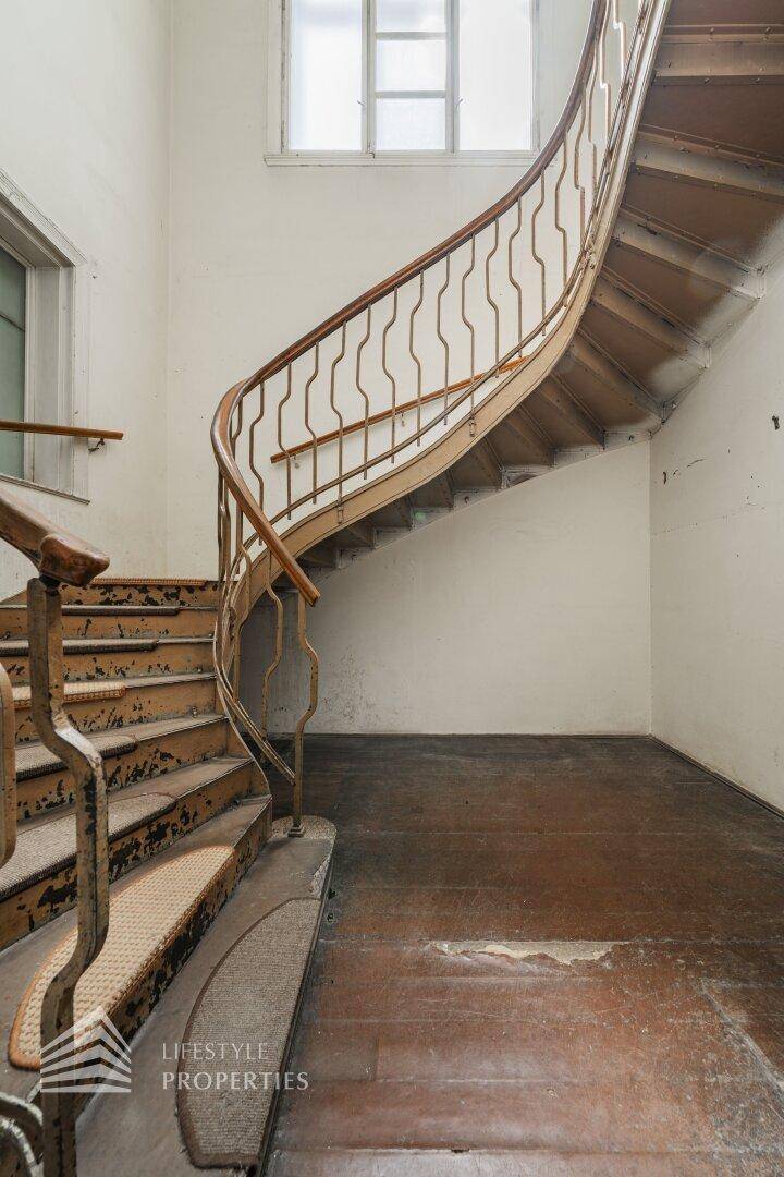 Elegante geschwungene Holztreppe mit kunstvollem Geländer in einem historischen Treppenhaus.