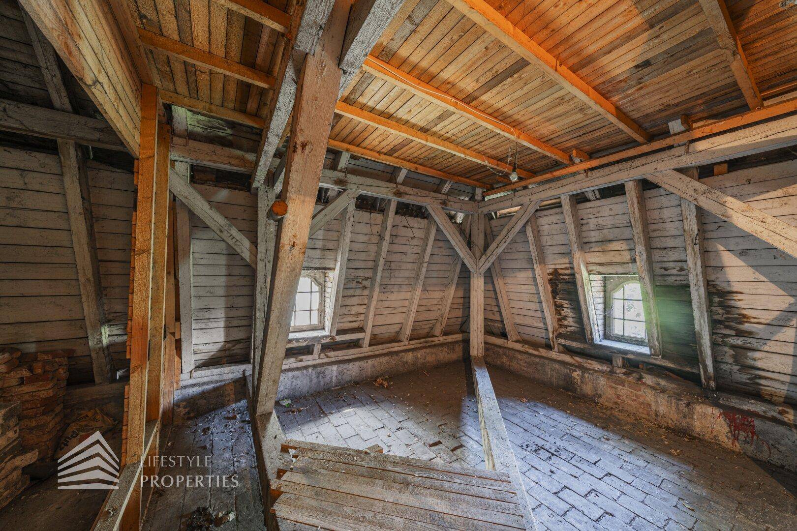 Unausgebauter Dachboden mit freiliegender Holzkonstruktion und kleinen Fenstern, bereit zur Renovierung.