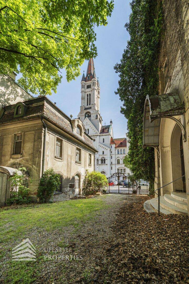 Historische Villa mit Blick auf eine imposante Kirche, umgeben von üppigem Grün und altem Baumbestand.