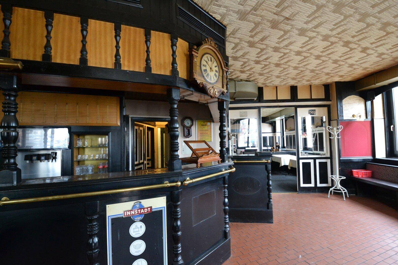 Traditionelle Bar mit dunklem Holz, einer großen Uhr und Terrakotta-Fliesenboden in einem Restaurant.