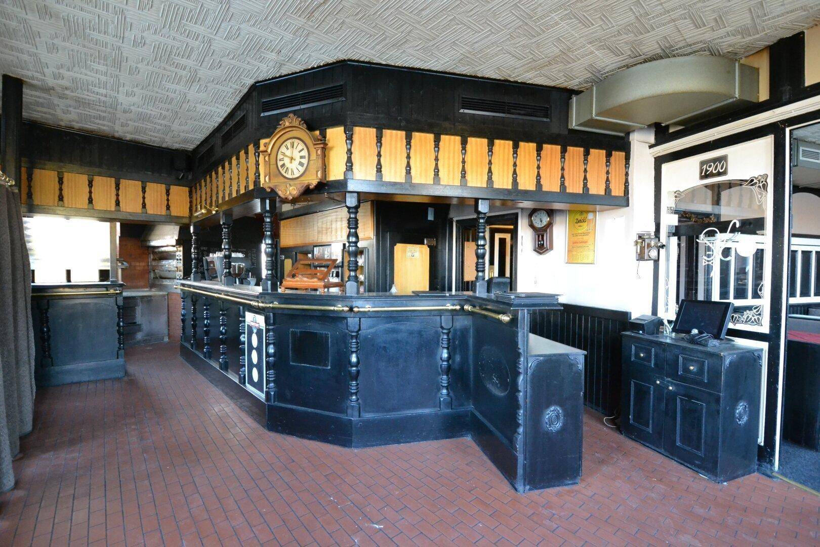 Detailansicht der traditionellen Bar mit Kasse, großer Uhr und dunklen Holzverzierungen im Gastraum.