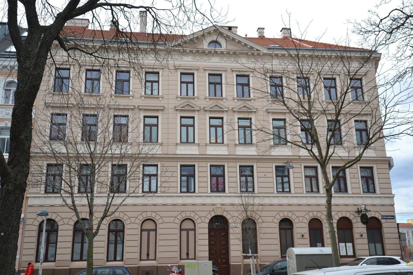 Historisches Mehrfamilienhaus mit klassischer Fassade, vielen Fenstern und Bäumen davor.