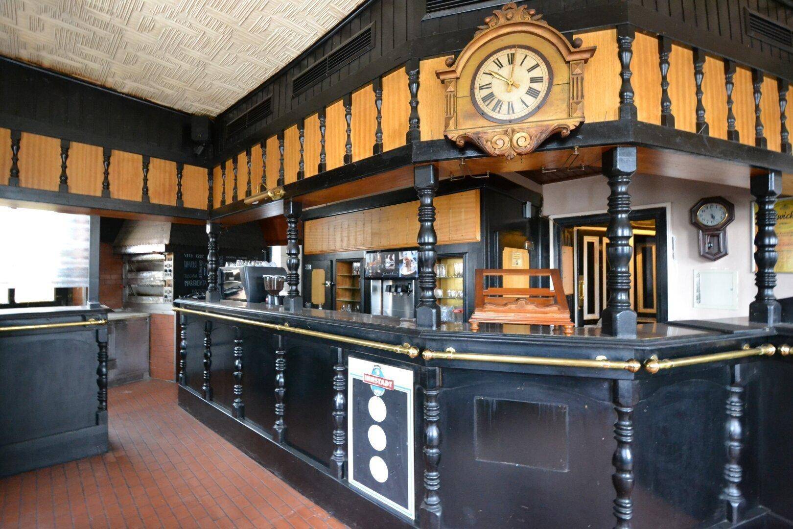 Traditionelle Bar mit dunklem Holz, einer großen Uhr und Terrakotta-Fliesenboden in einem Restaurant.