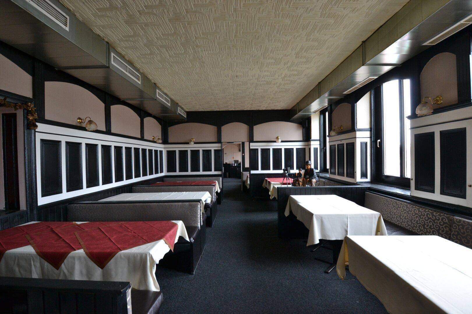 Langer Restaurantbereich mit Reihen von Tischen und gepolsterten Bänken, beleuchtet durch große Fenster.