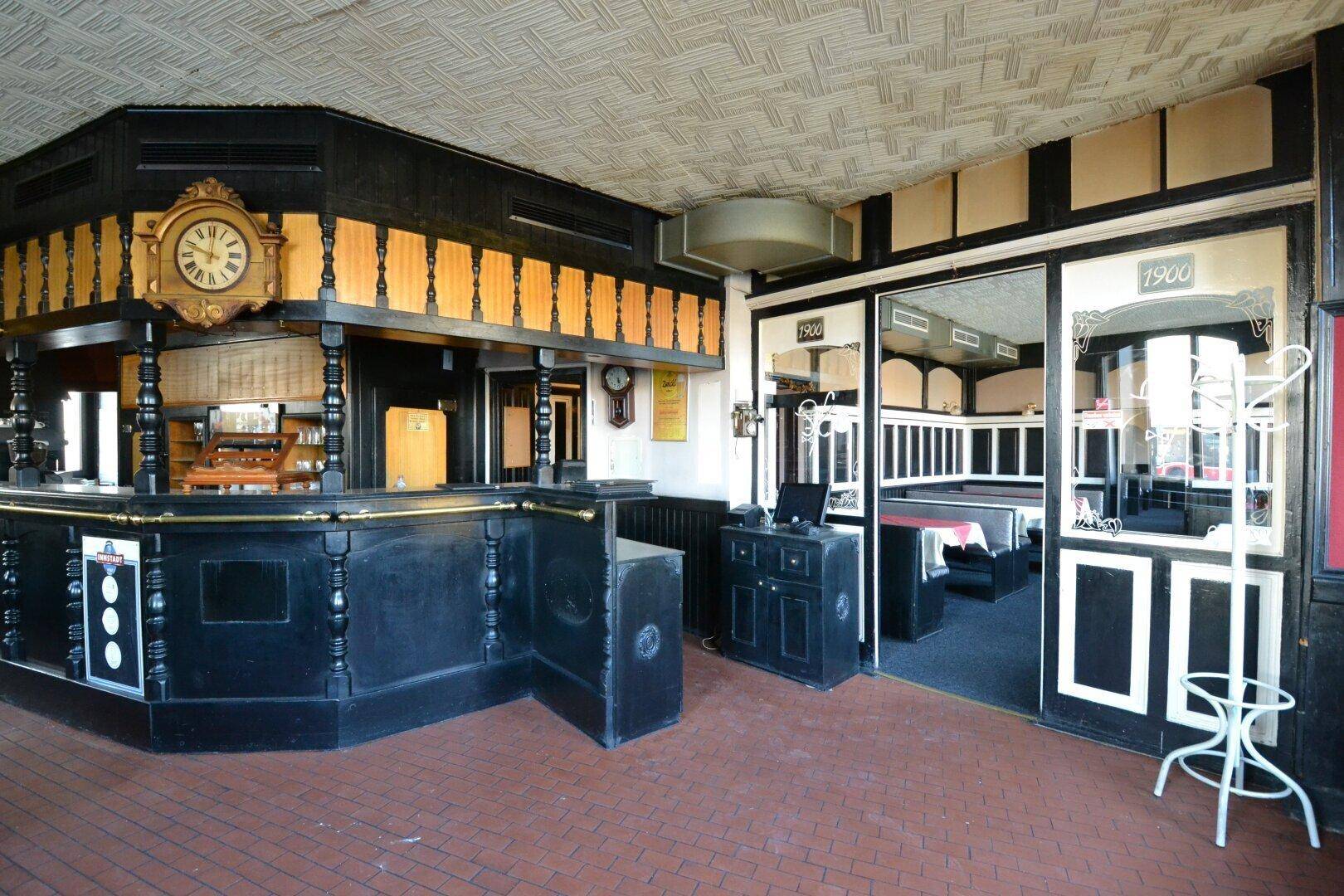 Traditioneller Barbereich mit dunklem Holz, einer großen Uhr und Blick auf den Eingangsbereich des Restaurants.