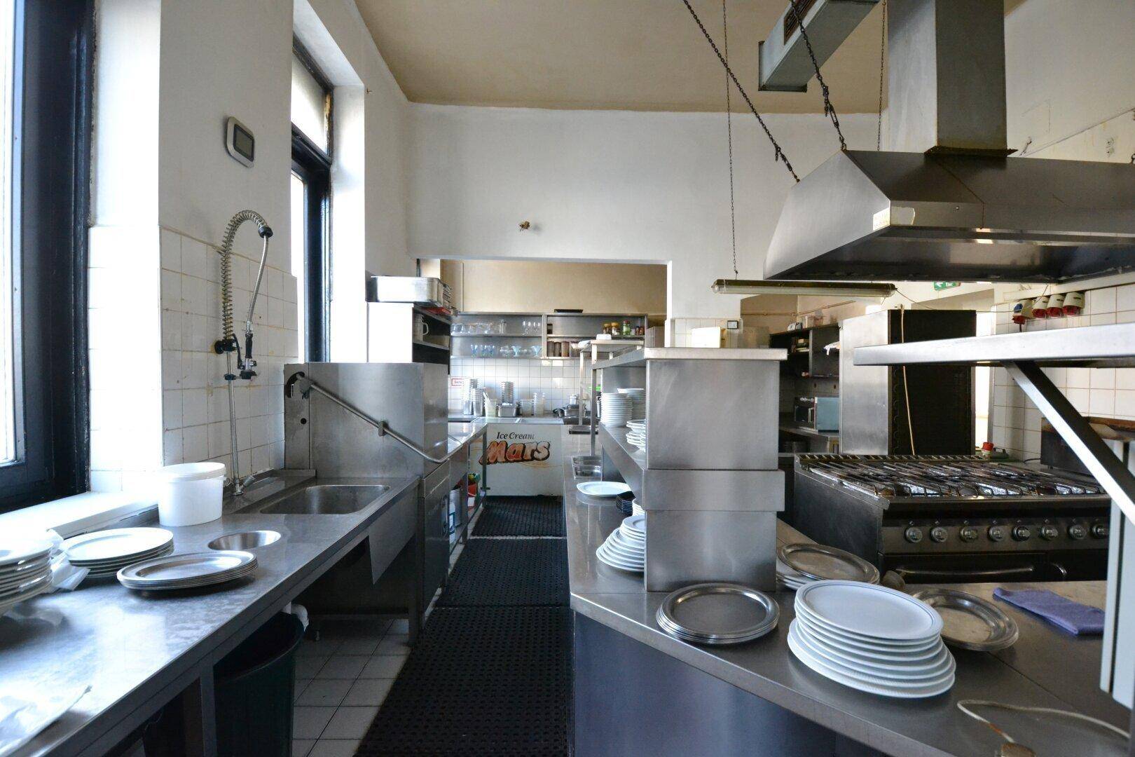 Professionelle Großküche mit Edelstahloberflächen, Spülbecken, Gasherd und Ablufthaube.