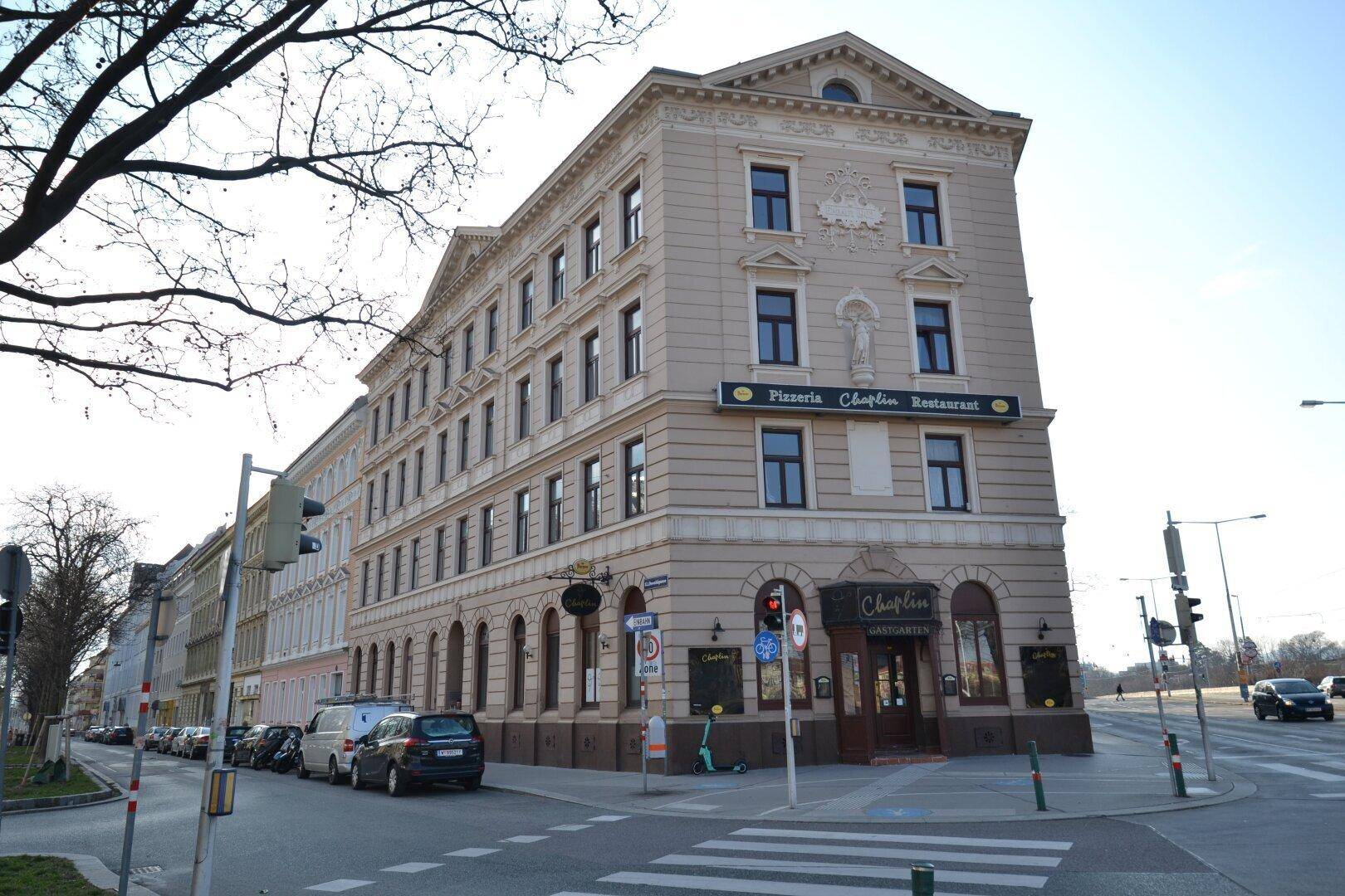 Historisches Eckgebäude mit klassischer Architektur, Geschäftsräumen im Erdgeschoss und umliegender Stadtansicht.